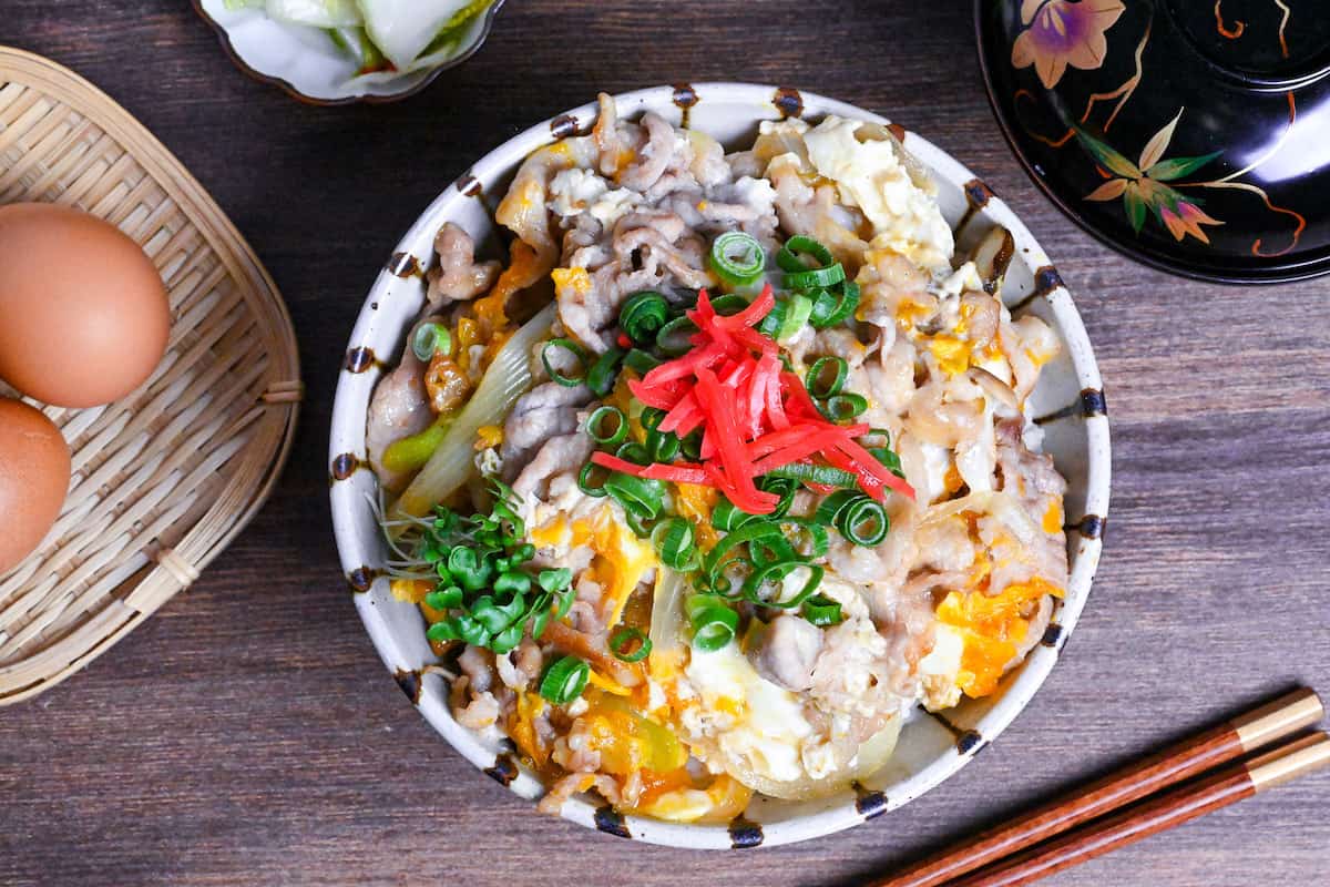 Tanin Don (Japanese pork and egg rice bowl) in a striped bowl topped with red pickled ginger and chopped green onions
