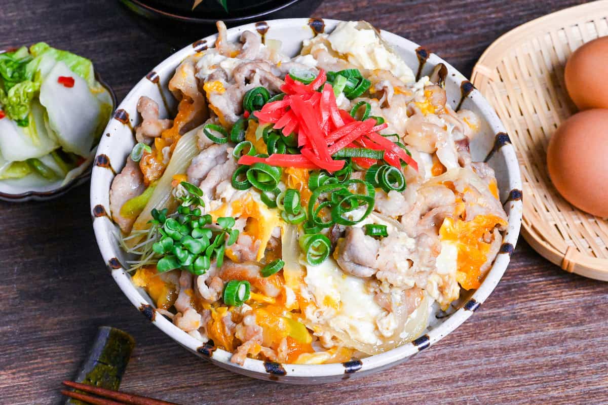Tanin Don (Japanese pork and egg rice bowl) in a striped bowl topped with red pickled ginger and chopped green onions