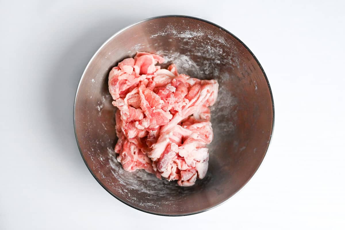 thinly sliced pork coated in thin layer of flour in a mixing bowl