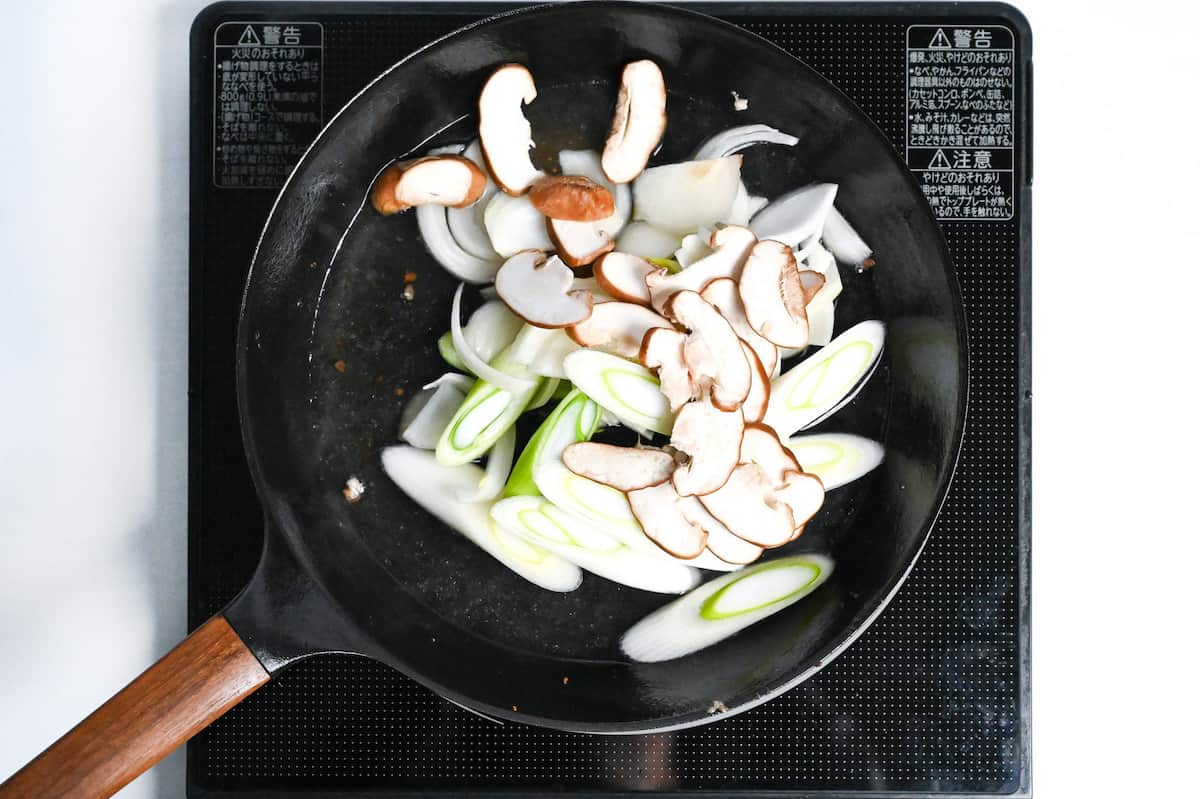 frying sliced Japanese leek (naganegi), yellow onion and fresh shiitake mushrooms in a pan