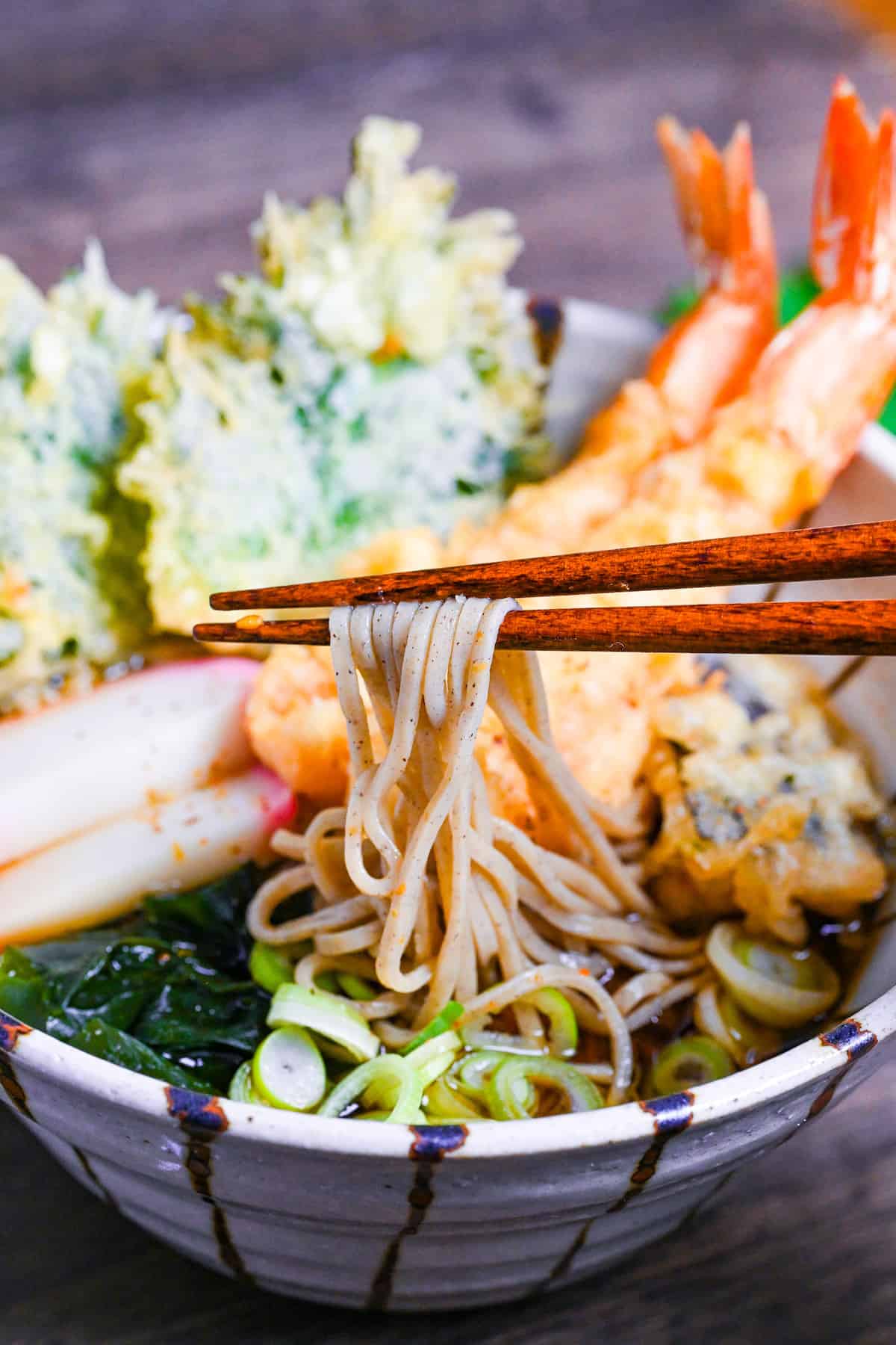 holding soba noodles with wooden chopsticks from a bowl of hot tempura soba