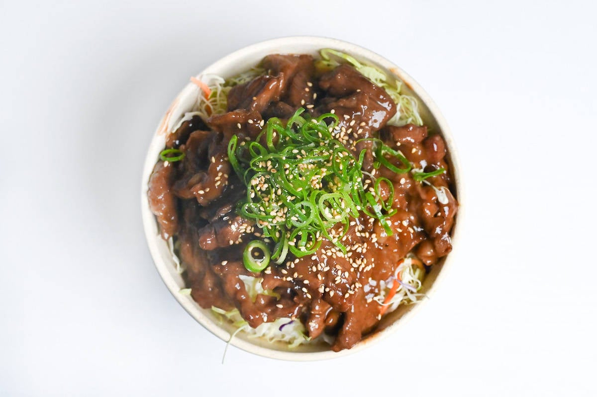 wasabi teriyaki beef over rice in a cream colored bowl and topped with green onions and sesame seeds