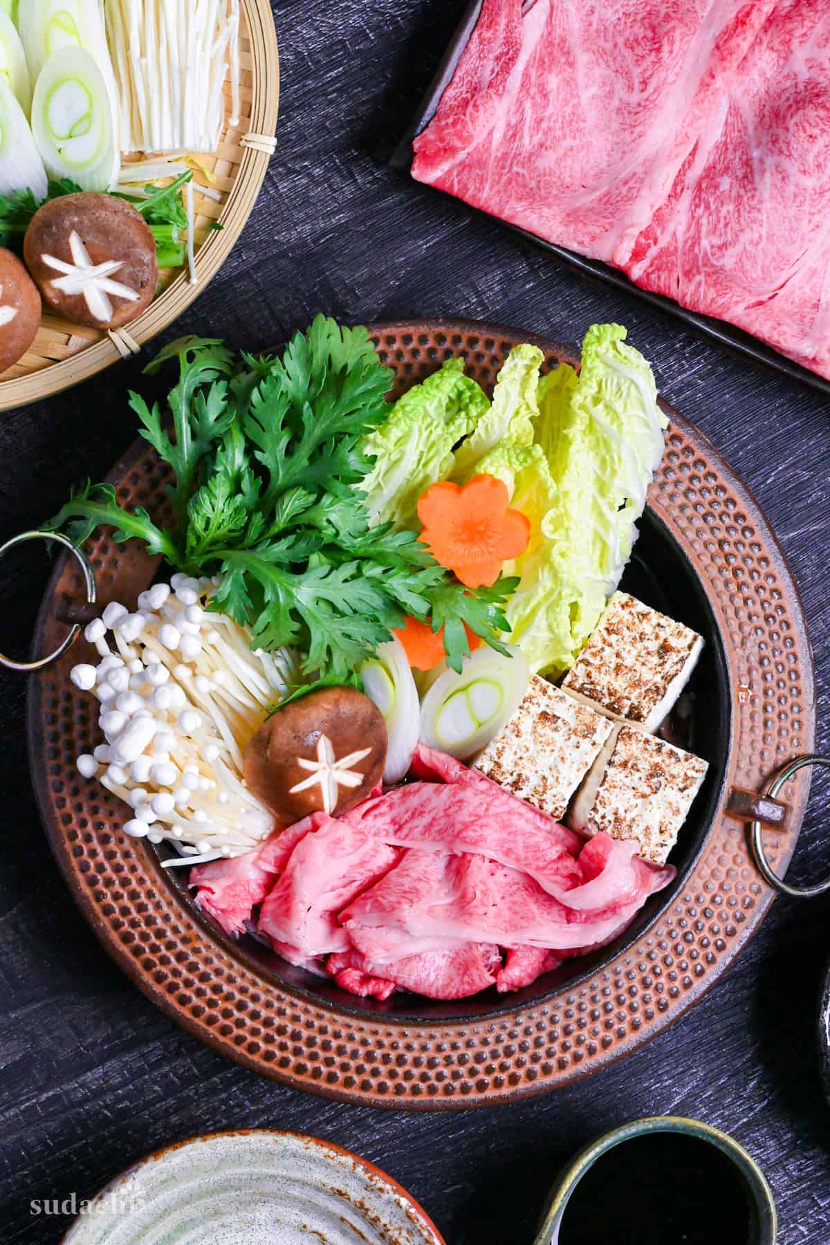 Traditional Japanese beef sukiyaki made with homemade sauce, thinly sliced wagyu beef, grilled tofu, shiitake mushrooms, enoki, carrots, napa cabbage, Japanese leeks and napa cabbage in a cast iron pot