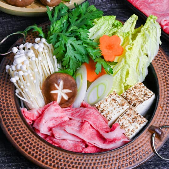 Traditional Japanese beef sukiyaki made with homemade sauce, thinly sliced wagyu beef, grilled tofu, shiitake mushrooms, enoki, carrots, napa cabbage, Japanese leeks and napa cabbage in a cast iron pot