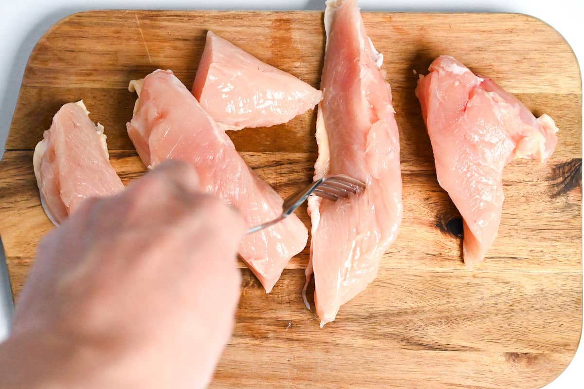 piercing chicken breast pieces with a fork to tenderize