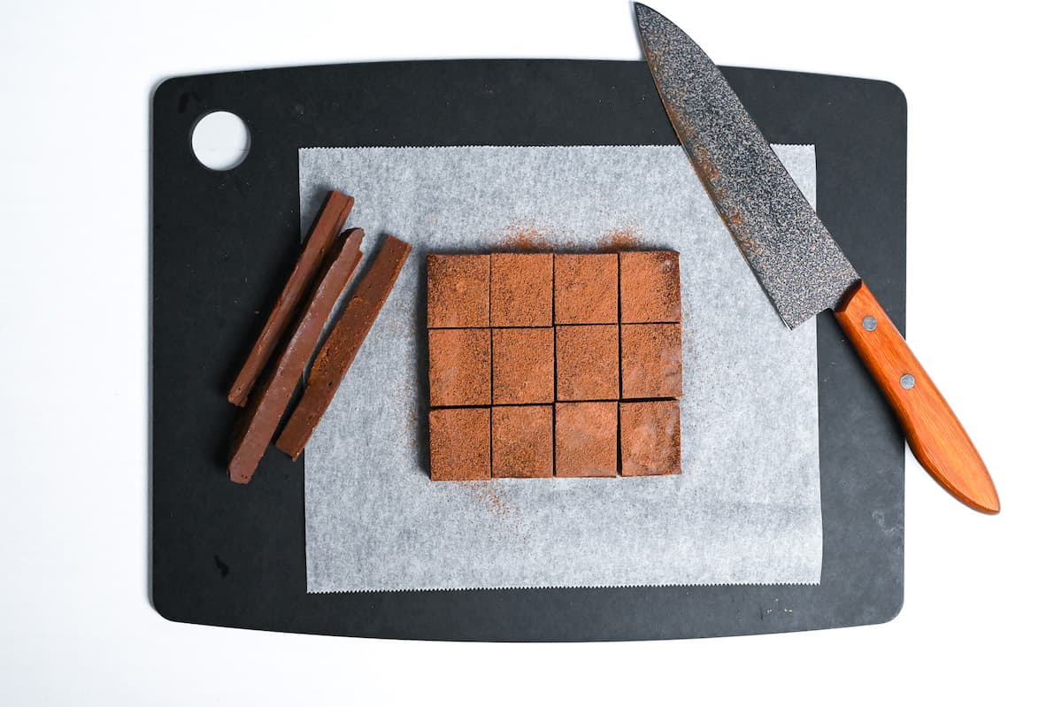set nama chocolate on a chopping board with edges trimmed, cut into 12 pieces and dusted with cocoa powder