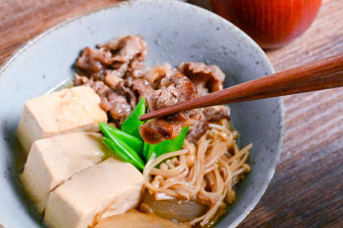holding a piece of beef from niku dofu with wooden chopsticks