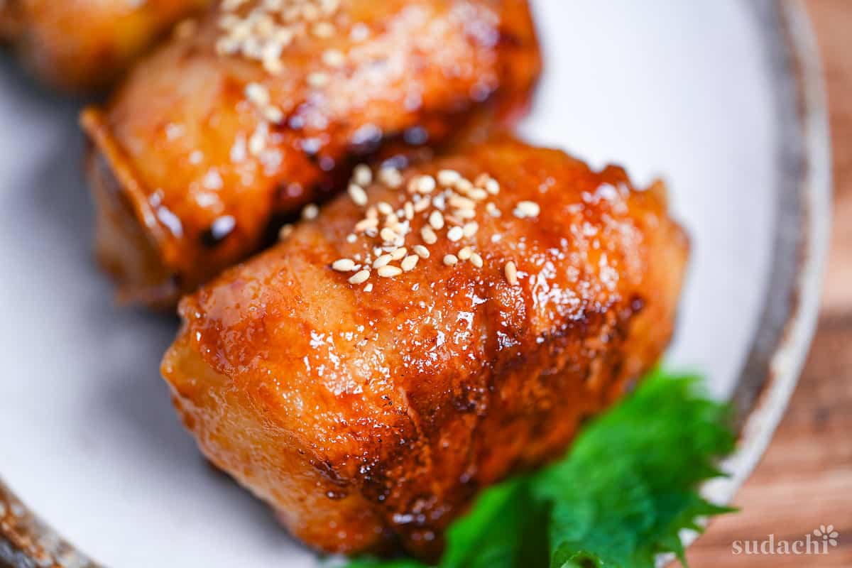 A close up of pan fried nikumaki onigiri (pork belly wrapped rice balls) sprinkled with sesame seeds