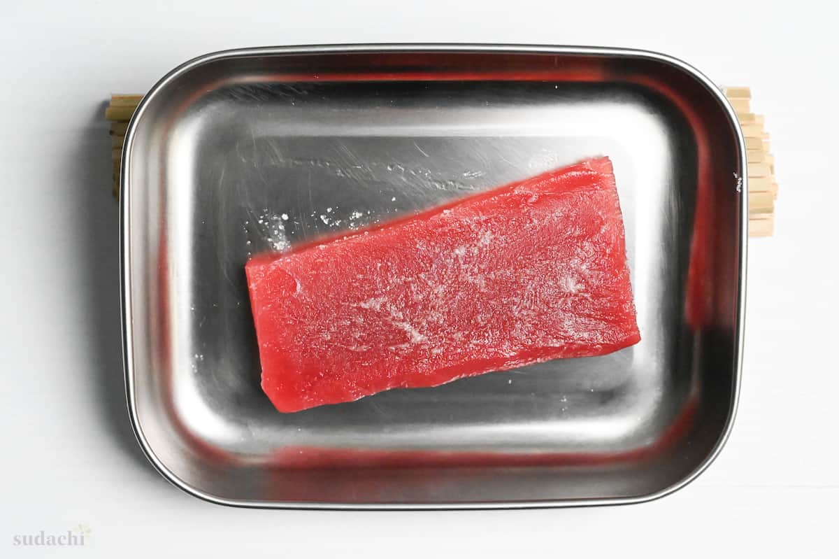 salted tuna sashimi block in a metal container draining on an incline