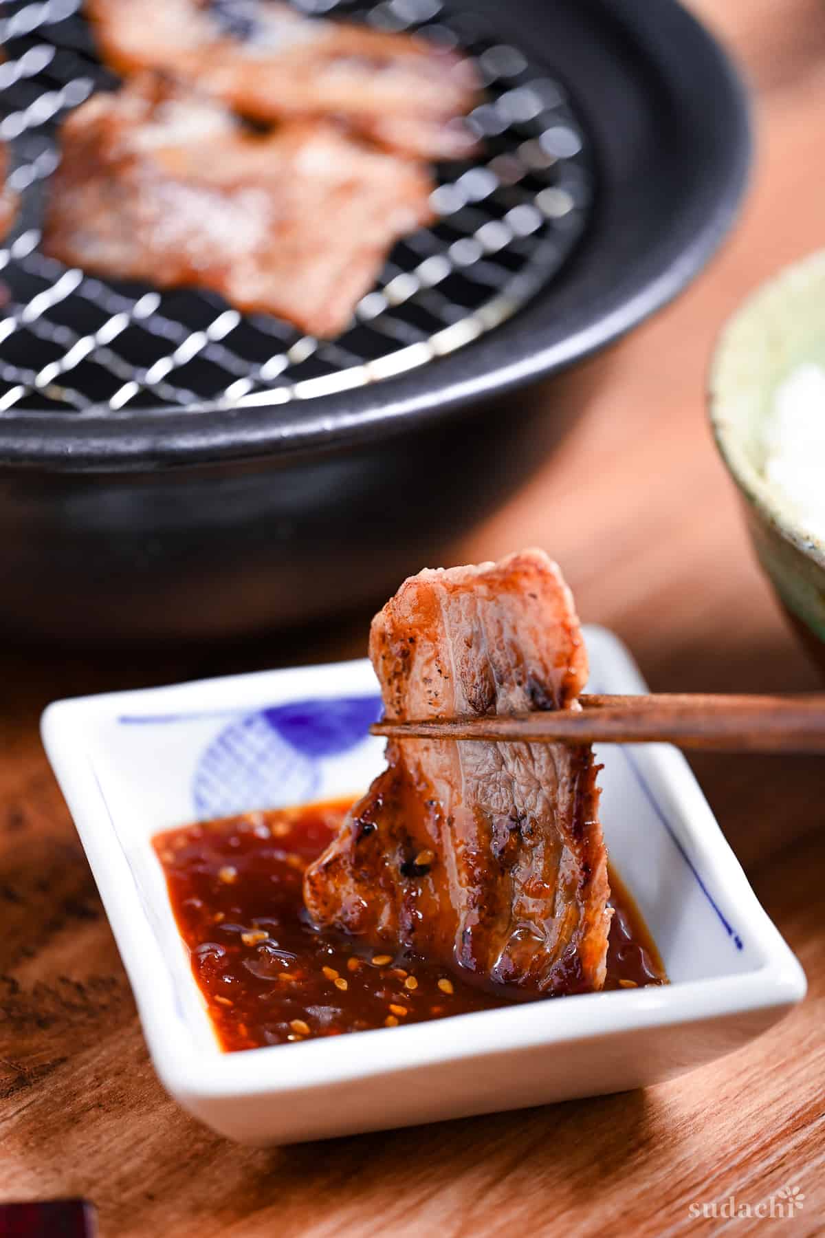 dipping a piece of thinly sliced beef in a white bowl of homemade yakiniku sauce