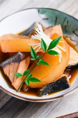 Buri Daikon (Simmered Yellowtail and Daikon Radish) in a small cream bowl with Japanese design topped with decorative leaves