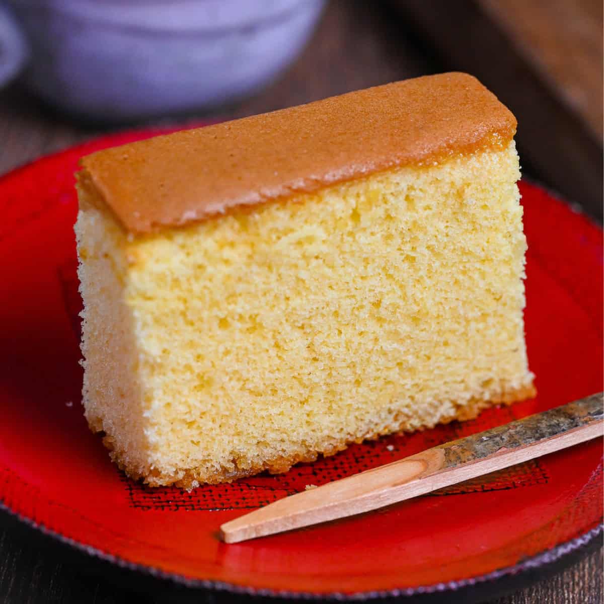 A single slice of Japanese castella sponge cake on a red lacquerware plate with wooden dessert pic