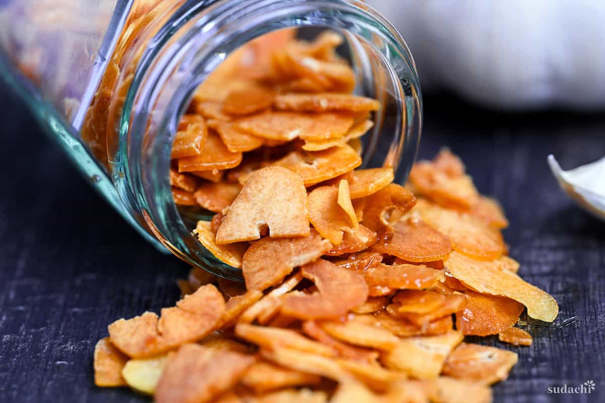 crispy garlic chips falling out of a glass jar onto a black wood-effect surface