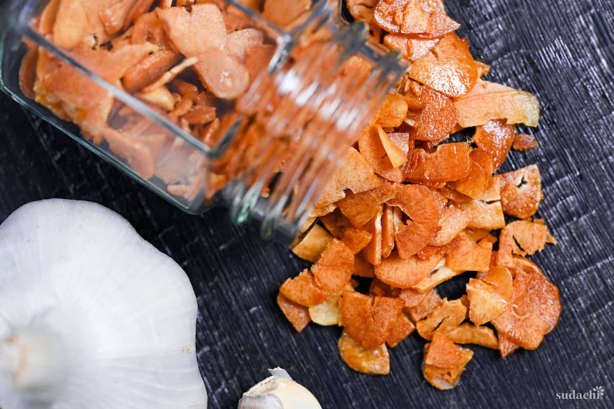 crispy garlic chips falling out of a glass jar onto a black wood-effect surface