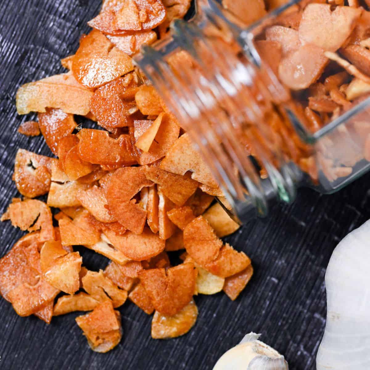 crispy garlic chips falling out of a glass jar onto a black wood-effect surface