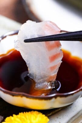 dipping a piece of kombu-cured sashimi-grade sea bream into a small fluted white bowl of soy sauce