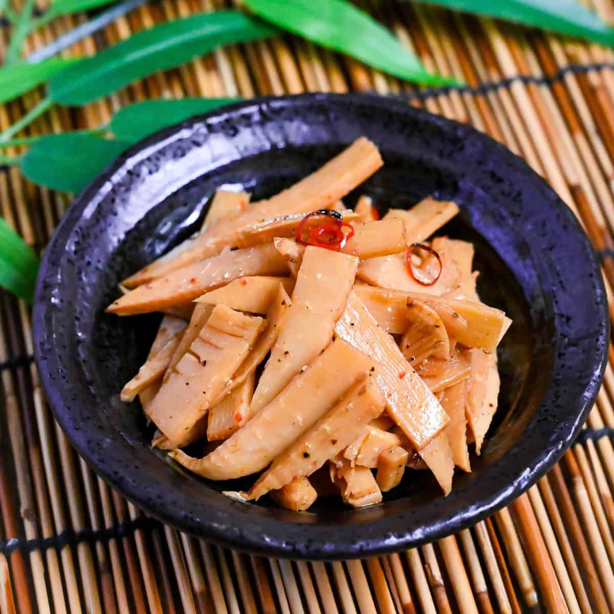 Menma-style seasoned bamboo shoots ramen topping in a black bowl on a bamboo background