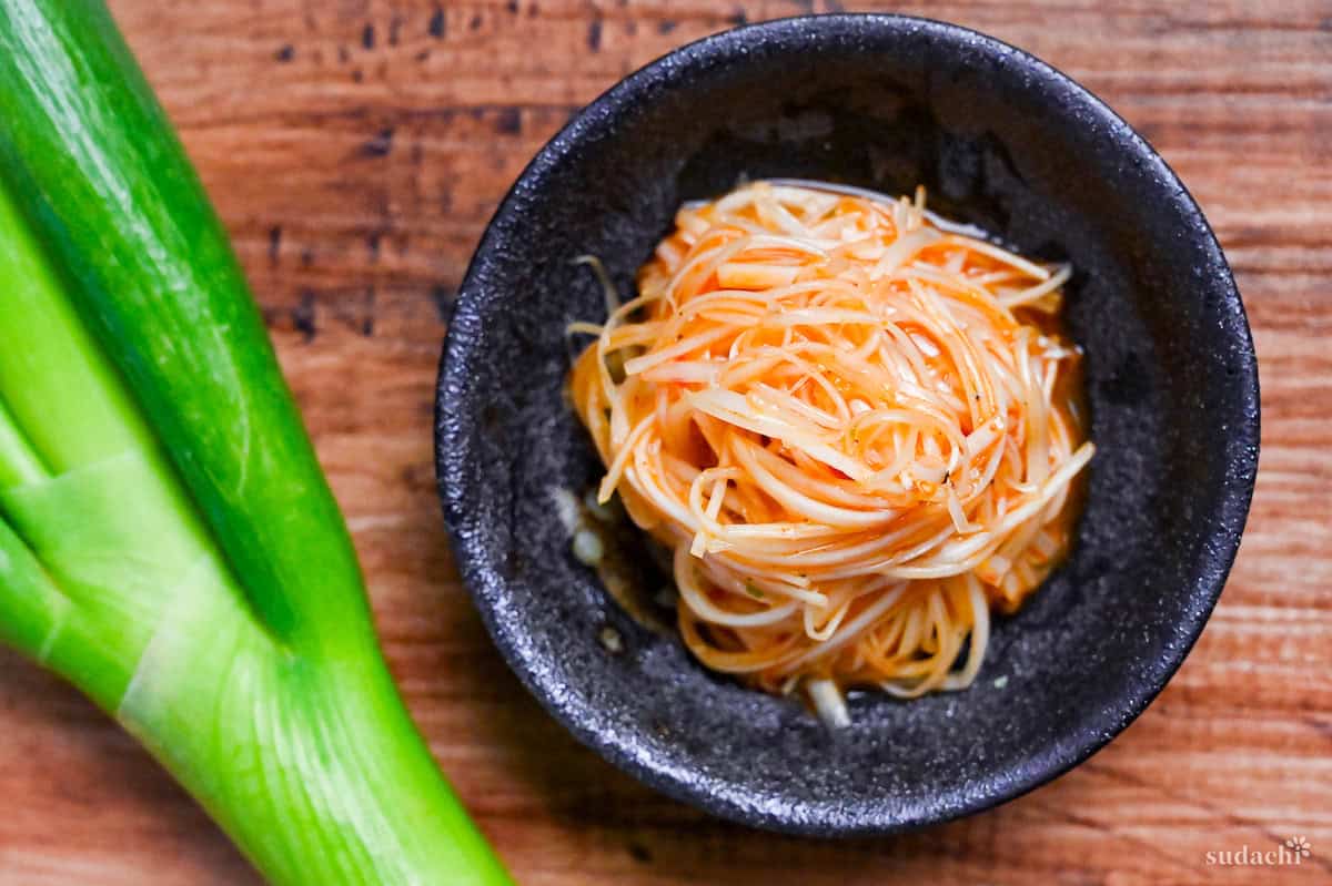 Spicy Negi (Strings of Japanese leek in a spicy dressing) in a black bowl on a wooden background