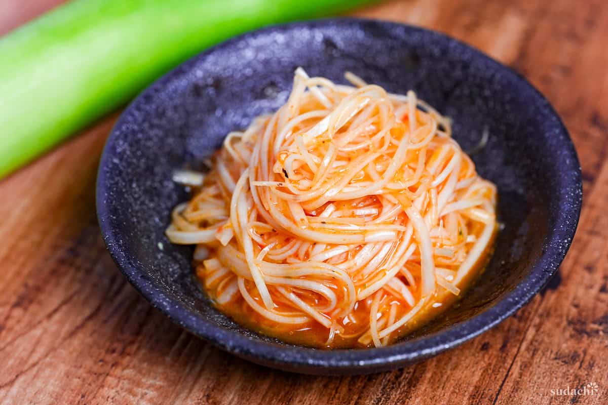 Spicy Negi (Strings of Japanese leek in a spicy dressing) in a black bowl on a wooden background
