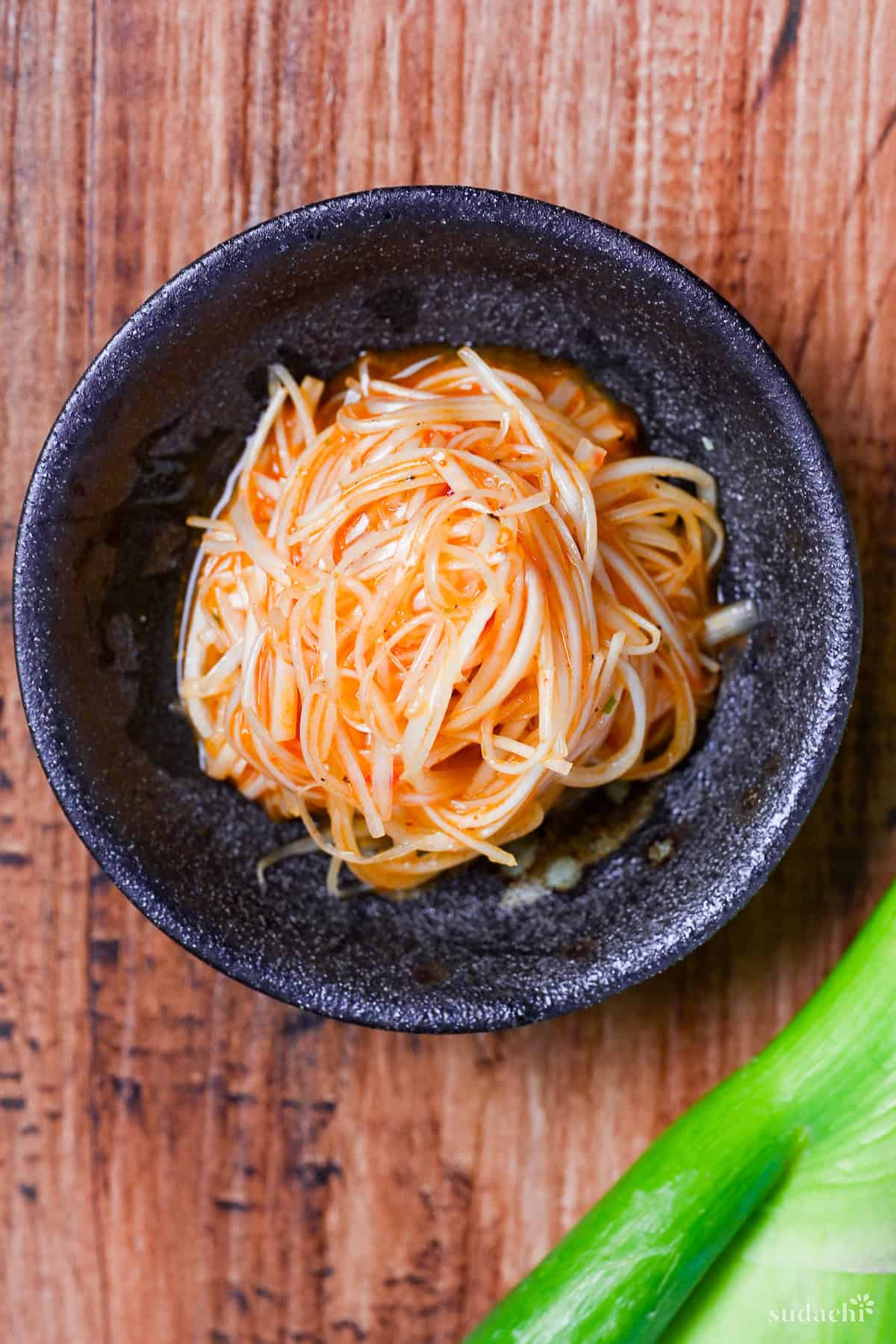 Spicy Negi (Strings of Japanese leek in a spicy dressing) in a black bowl on a wooden background