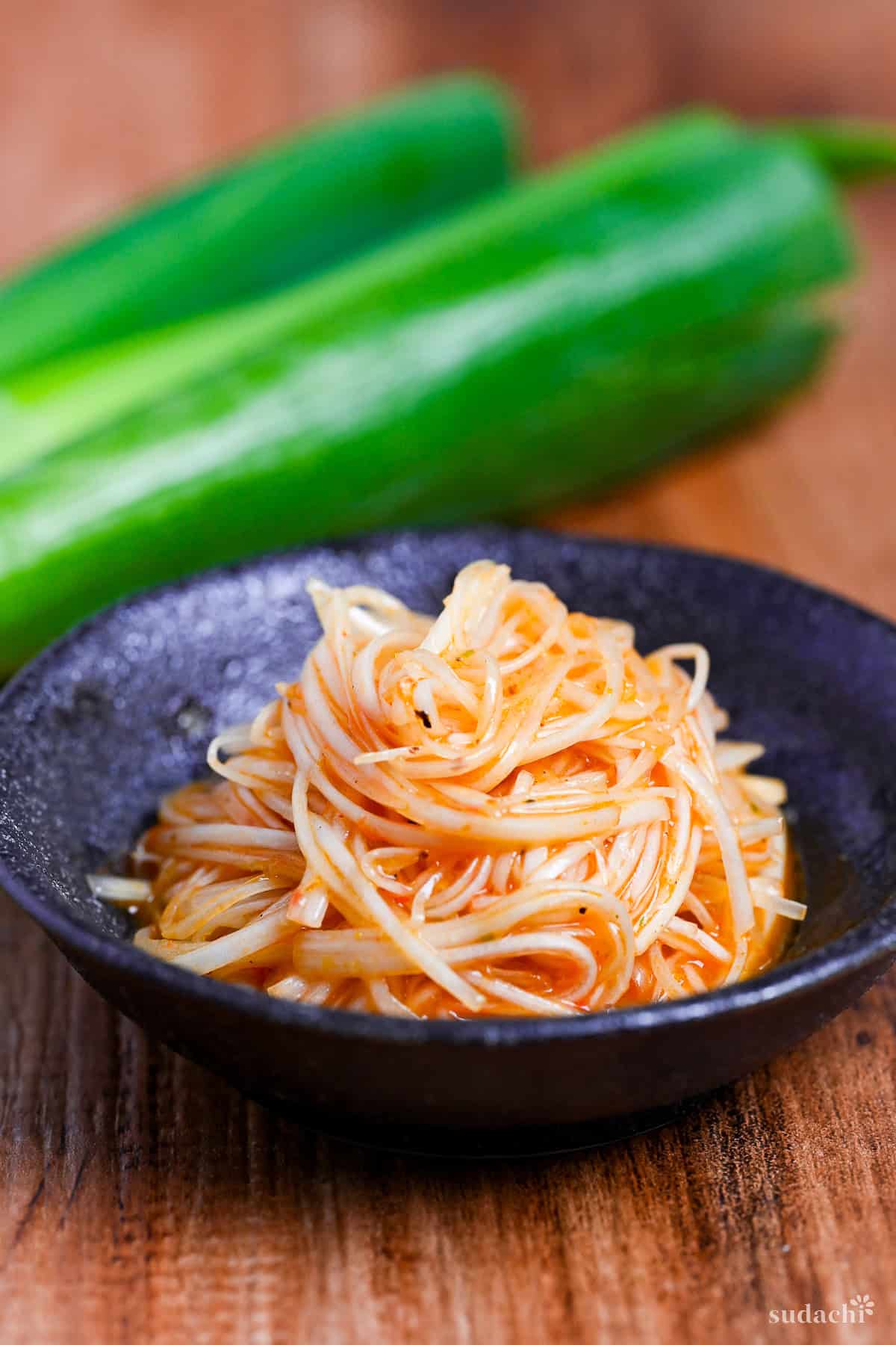 Spicy Negi (Strings of Japanese leek in a spicy dressing) in a black bowl on a wooden background