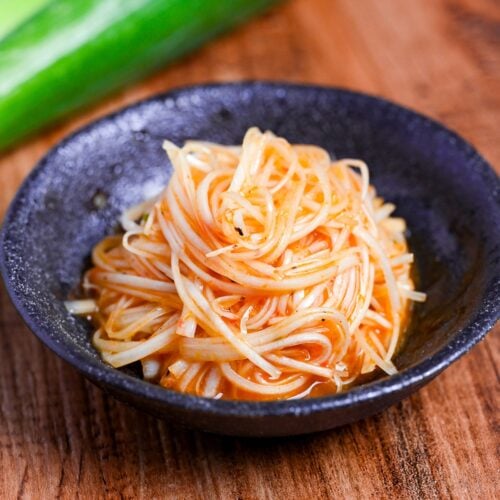 Spicy Negi (Strings of Japanese leek in a spicy dressing) in a black bowl on a wooden background