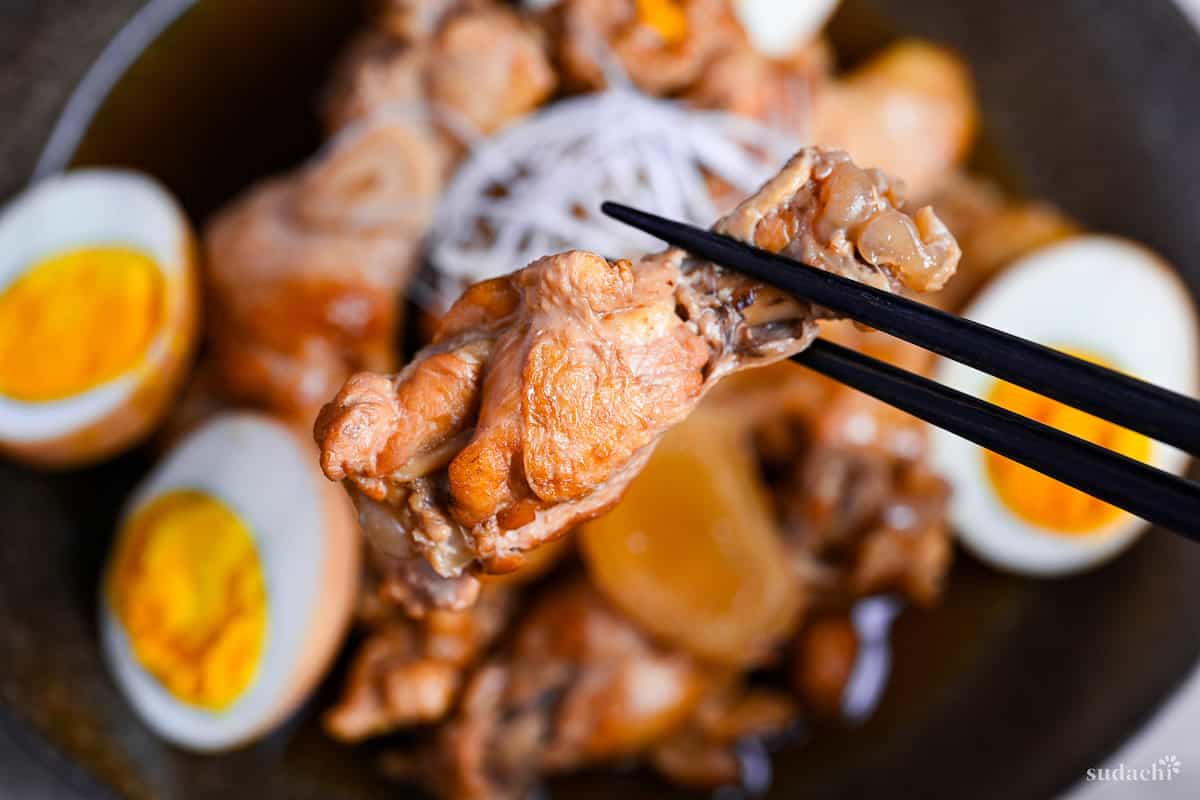 holding a simmered chicken drumstick with black chopsticks