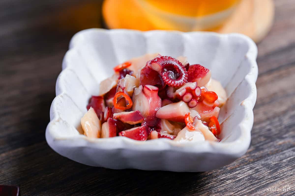 Wasabi-marinated octopus (tako wasa) in a square white bowl with fluted edges on a dark wooden surface