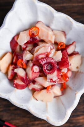 Wasabi-marinated octopus (tako wasa) in a square white bowl with fluted edges on a dark wooden surface