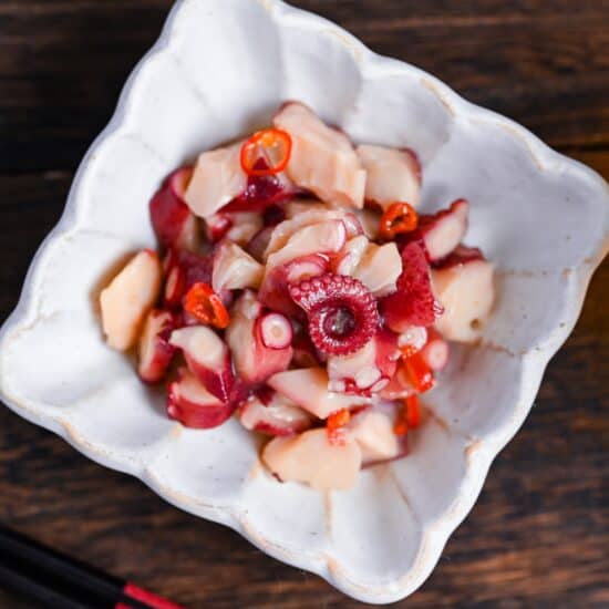 Wasabi-marinated octopus (tako wasa) in a square white bowl with fluted edges on a dark wooden surface