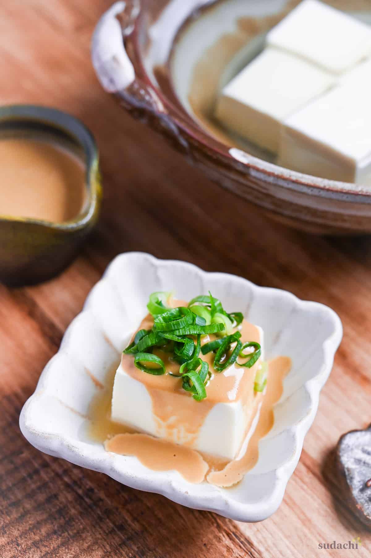 Yudofu simmered tofu drizzled with homemade sesame sauce topped with chopped green onions in a square white fluted bowl