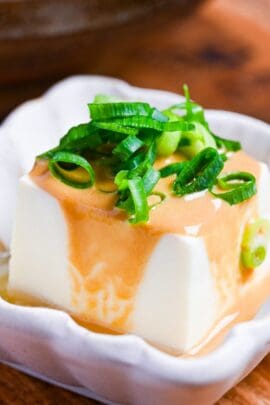 Yudofu simmered tofu drizzled with homemade sesame sauce topped with chopped green onions in a square white fluted bowl