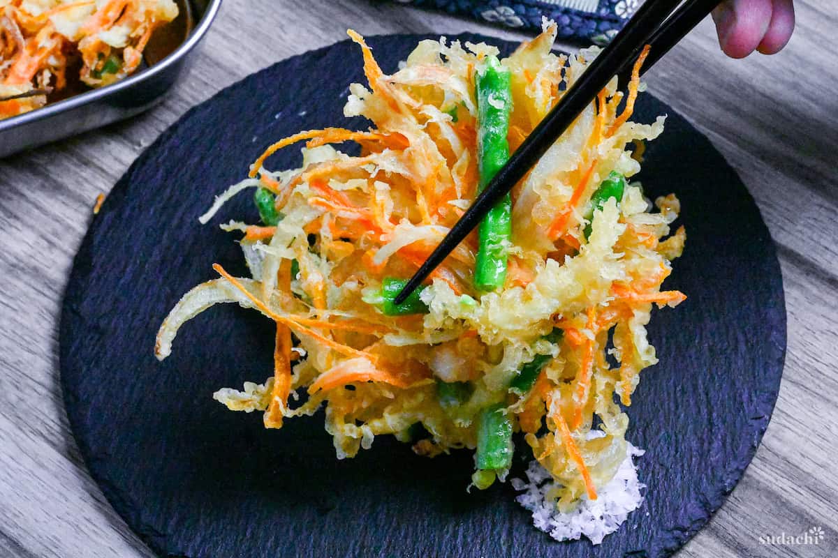 holding kakiage (Japanese mixed vegetable tempura) with black chopsticks and dipping in coarse salt