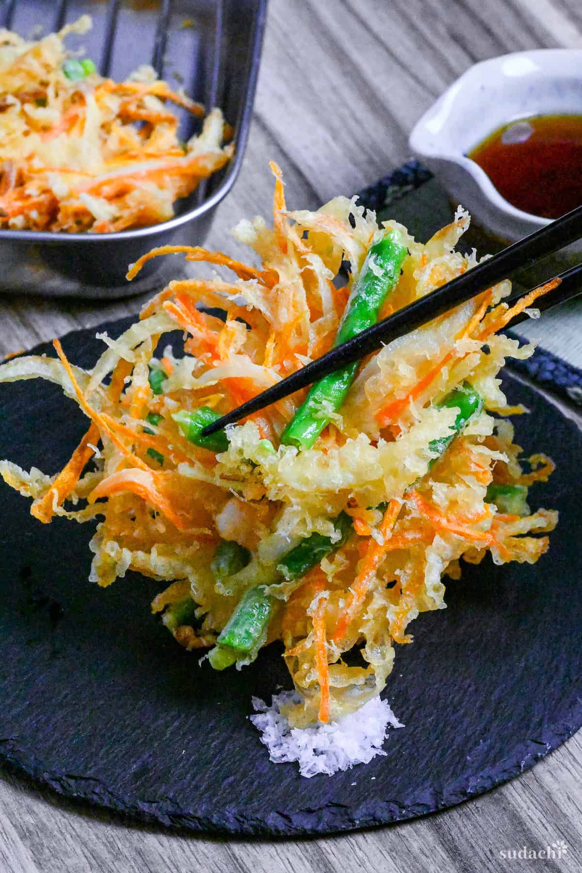 holding kakiage (Japanese mixed vegetable tempura) with black chopsticks and dipping in coarse salt