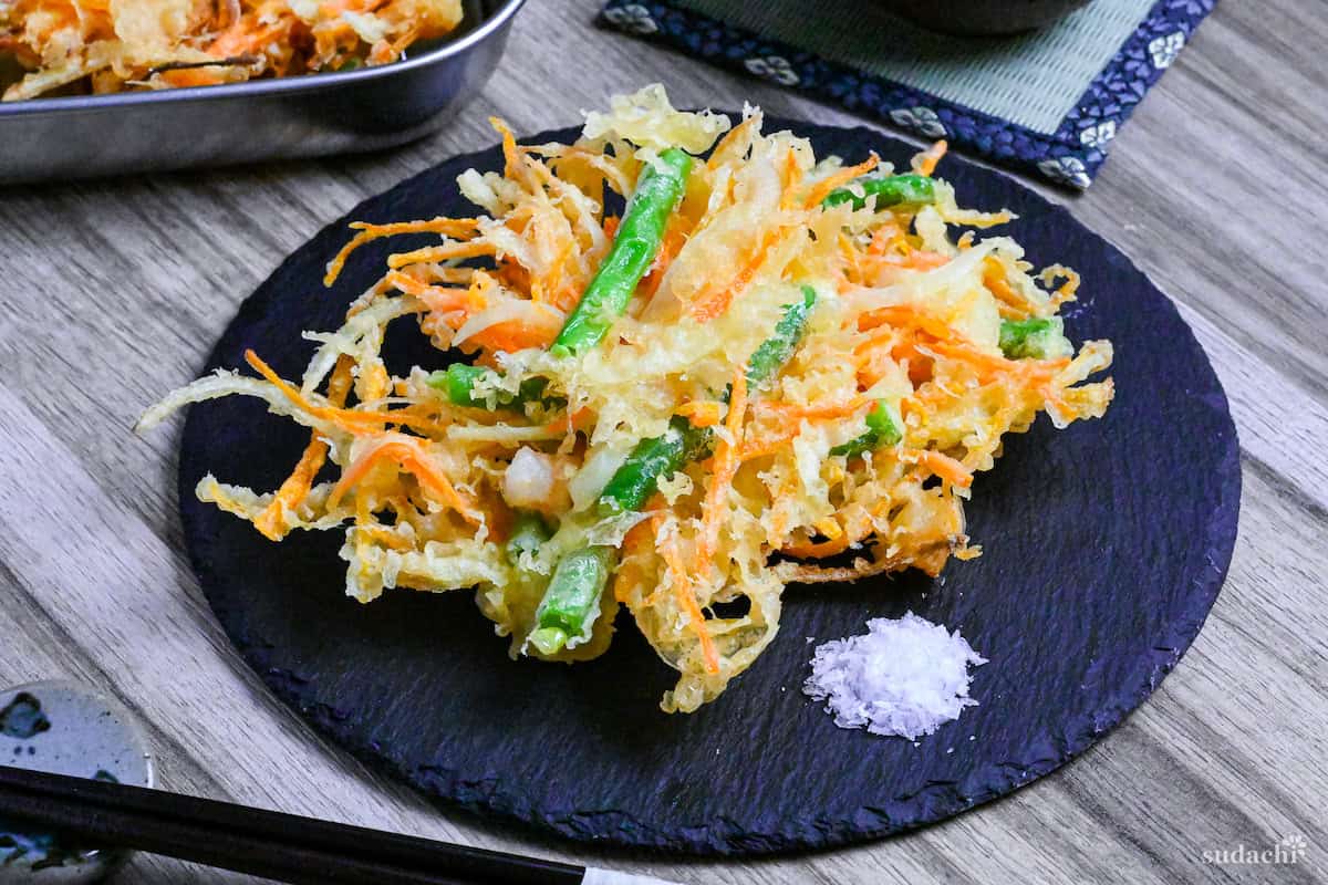 Kakiage (Japanese mixed vegetable tempura) on a slate plate next to a small heap of coarse salt for dipping