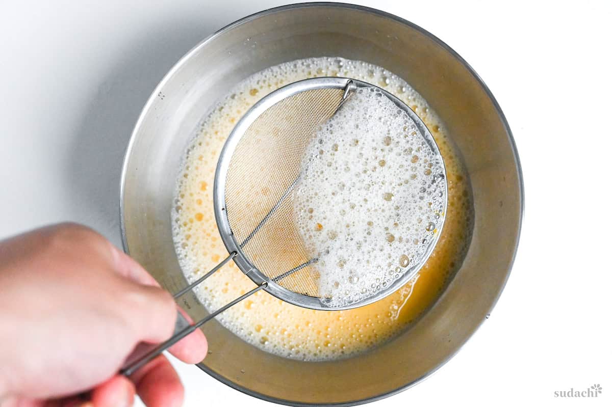 scooping bubbles out of whisked egg mixture