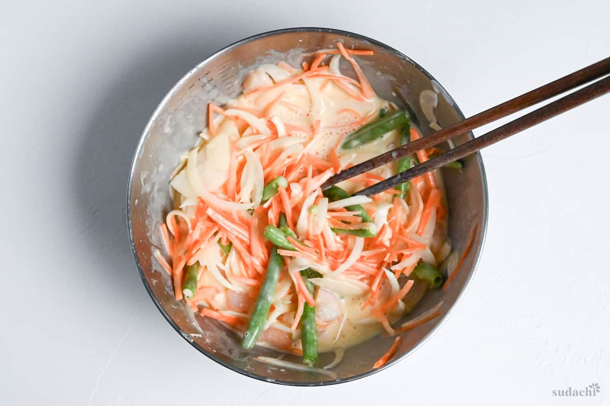 Mixed vegetables and shrimp in tempura batter in a metal bowl mixed with wooden chopsticks