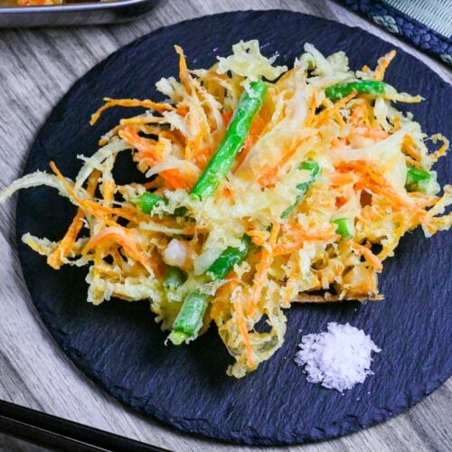 Kakiage (Japanese mixed vegetable tempura) on a slate plate next to a small heap of coarse salt for dipping