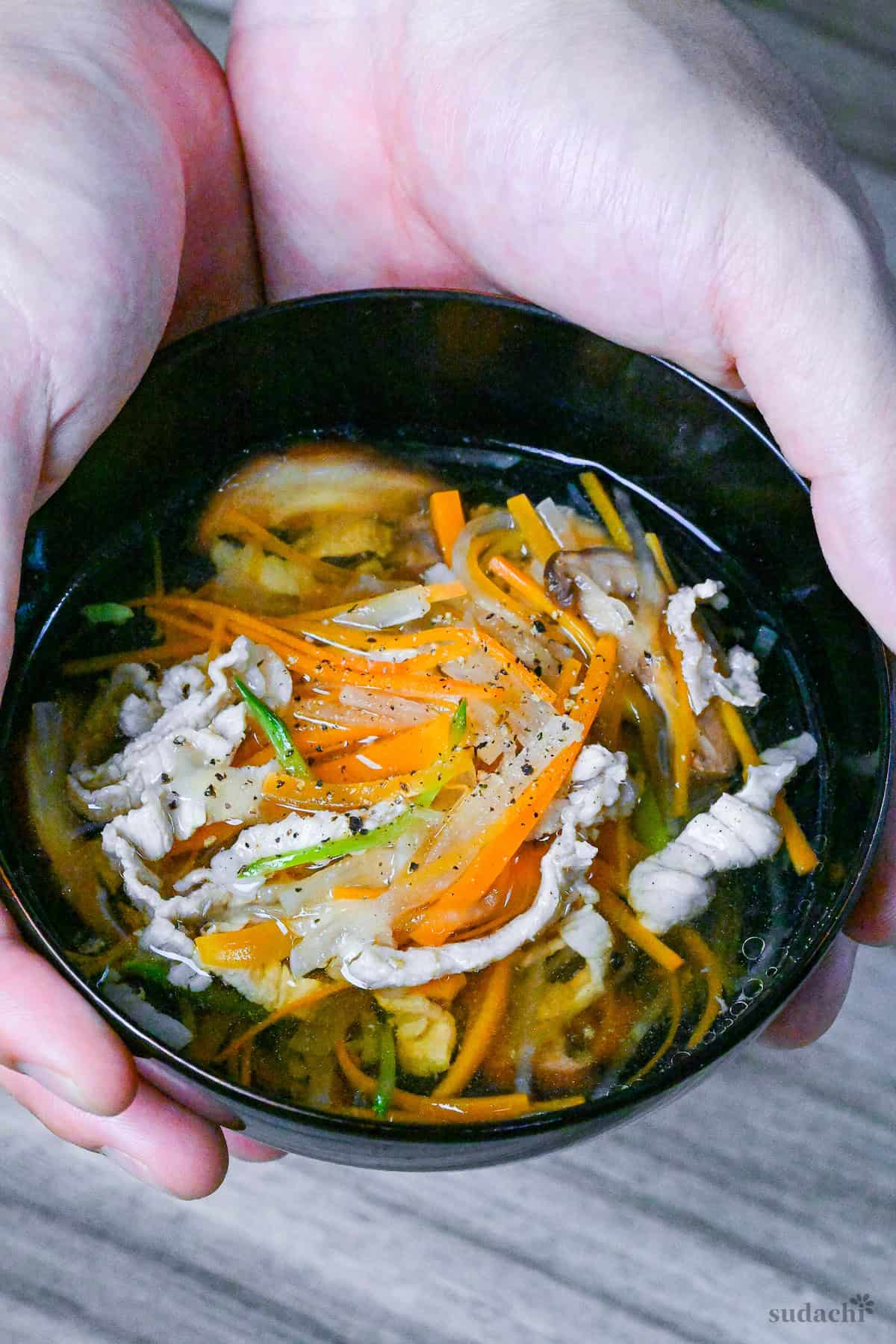 Sawaniwan (Japanese pork and vegetable soup) in a black bowl held with two hands