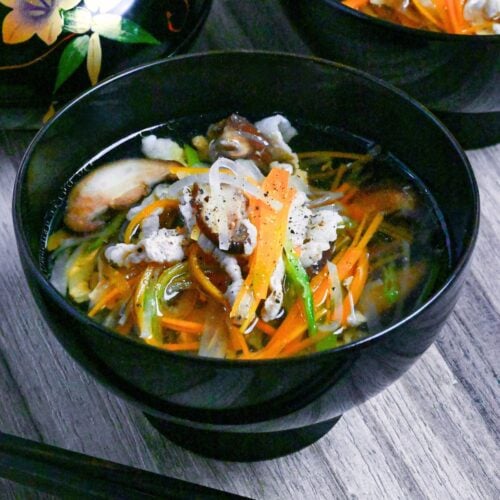 Sawaniwan (Japanese pork and vegetable soup) in a black bowl on a ashy wood background