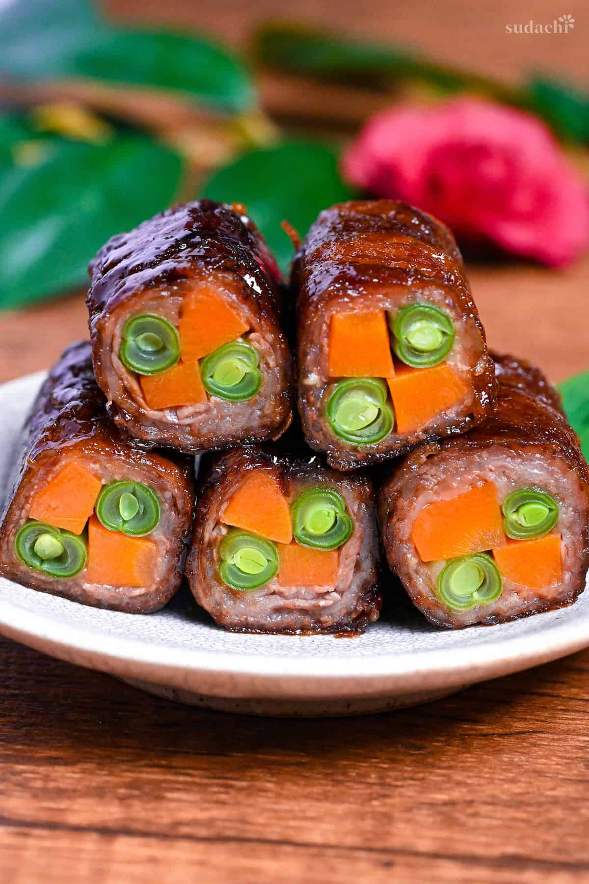 Beef yawatamaki (beef rolls with carrot and green beans) stacked on a white plate with perilla leaf