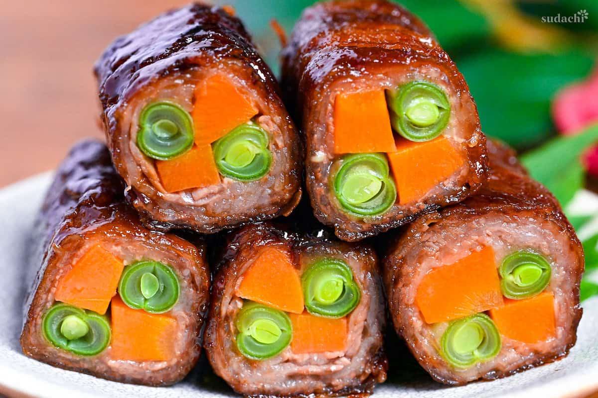 Beef yawatamaki (beef rolls with carrot and green beans) stacked on a white plate with perilla leaf
