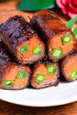 Beef yawatamaki (beef rolls with carrot and green beans) stacked on a white plate with perilla leaf