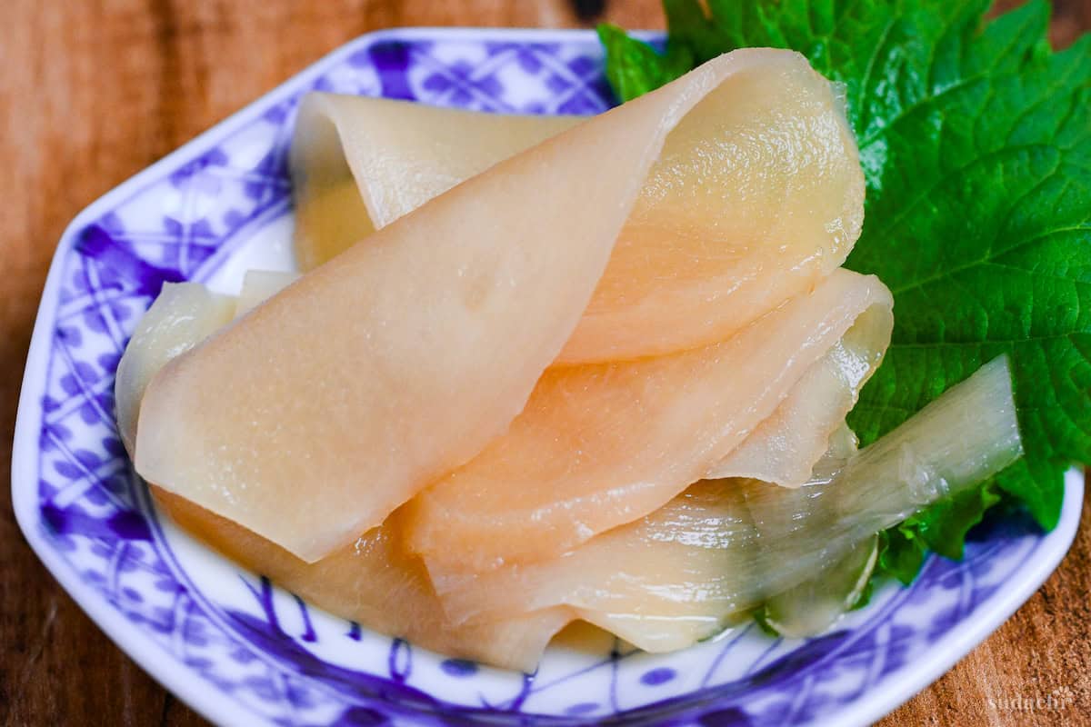 close up of Homemade gari (Japanese pickled sushi ginger) on a white and blue plate decorated with a Perilla leaf on a wooden background