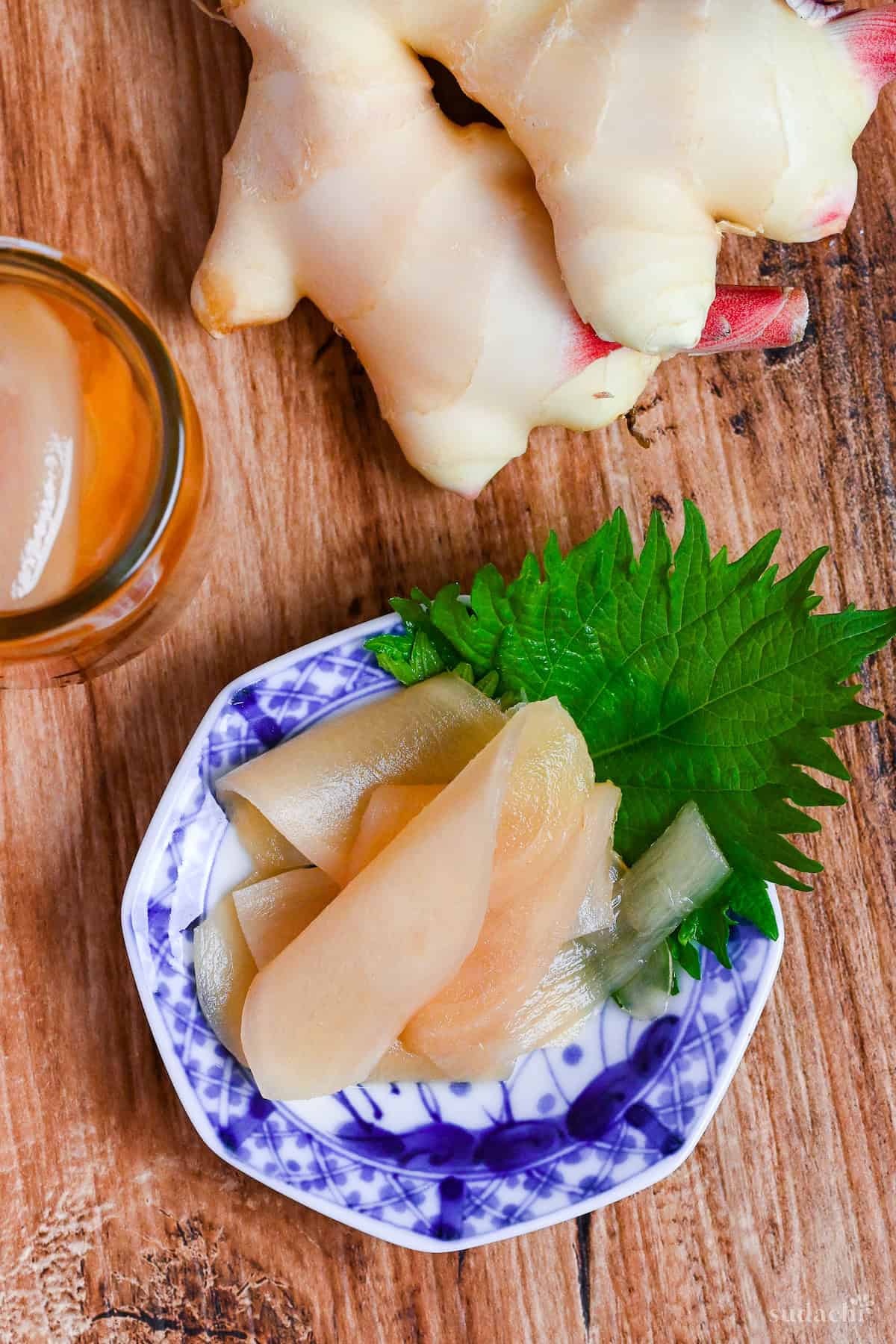 Homemade gari (Japanese pickled sushi ginger) on a white and blue plate decorated with a Perilla leaf on a wooden background