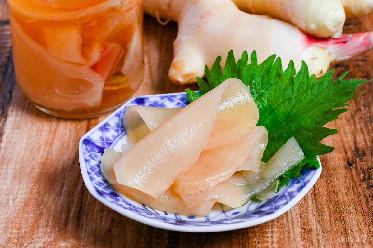 Homemade gari (Japanese pickled sushi ginger) on a white and blue plate decorated with a Perilla leaf on a wooden background