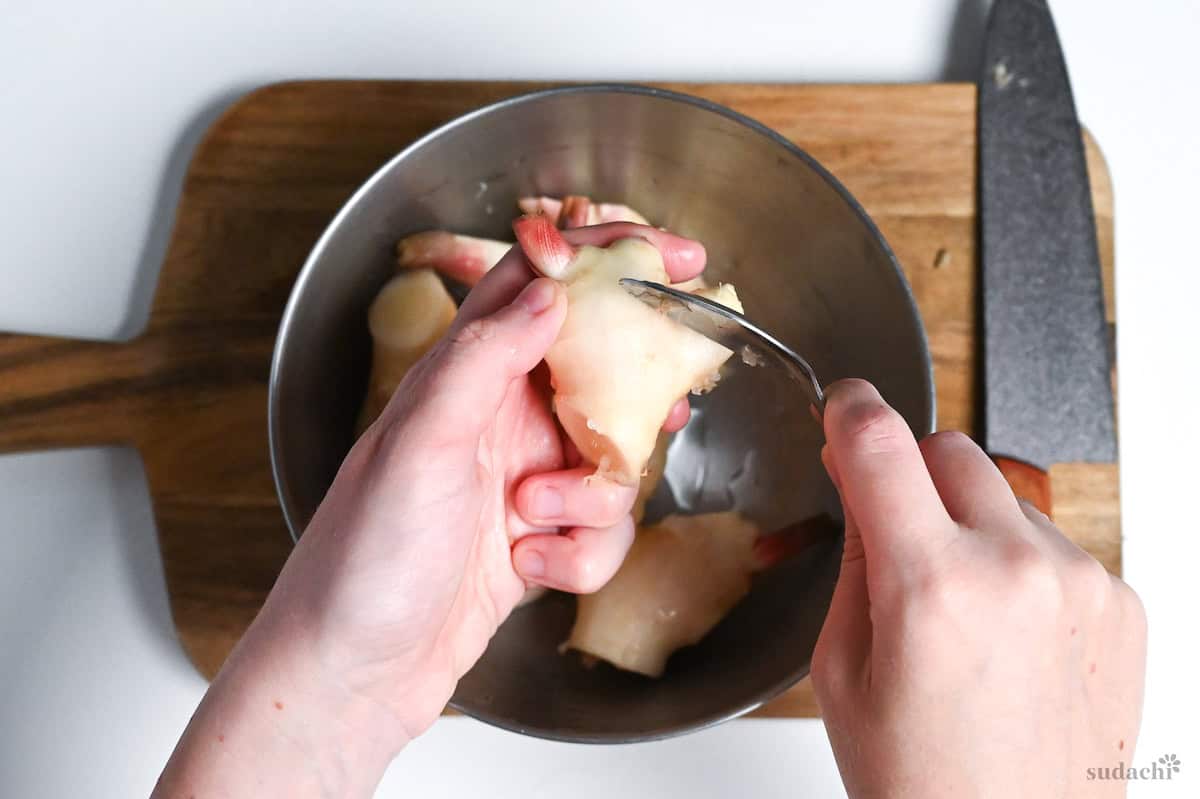 scraping the skin off the surface of young ginger with a spoon