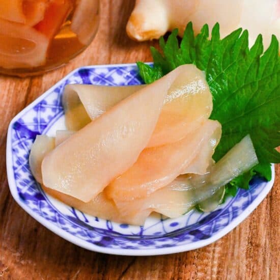 Homemade gari (Japanese pickled sushi ginger) on a white and blue plate decorated with a Perilla leaf on a wooden background