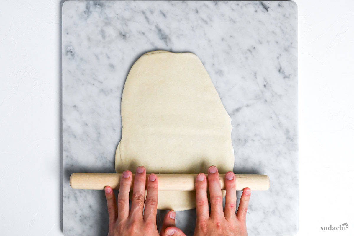 rolling out ramen noodle dough with a wooden rolling pin on a marble kneading board