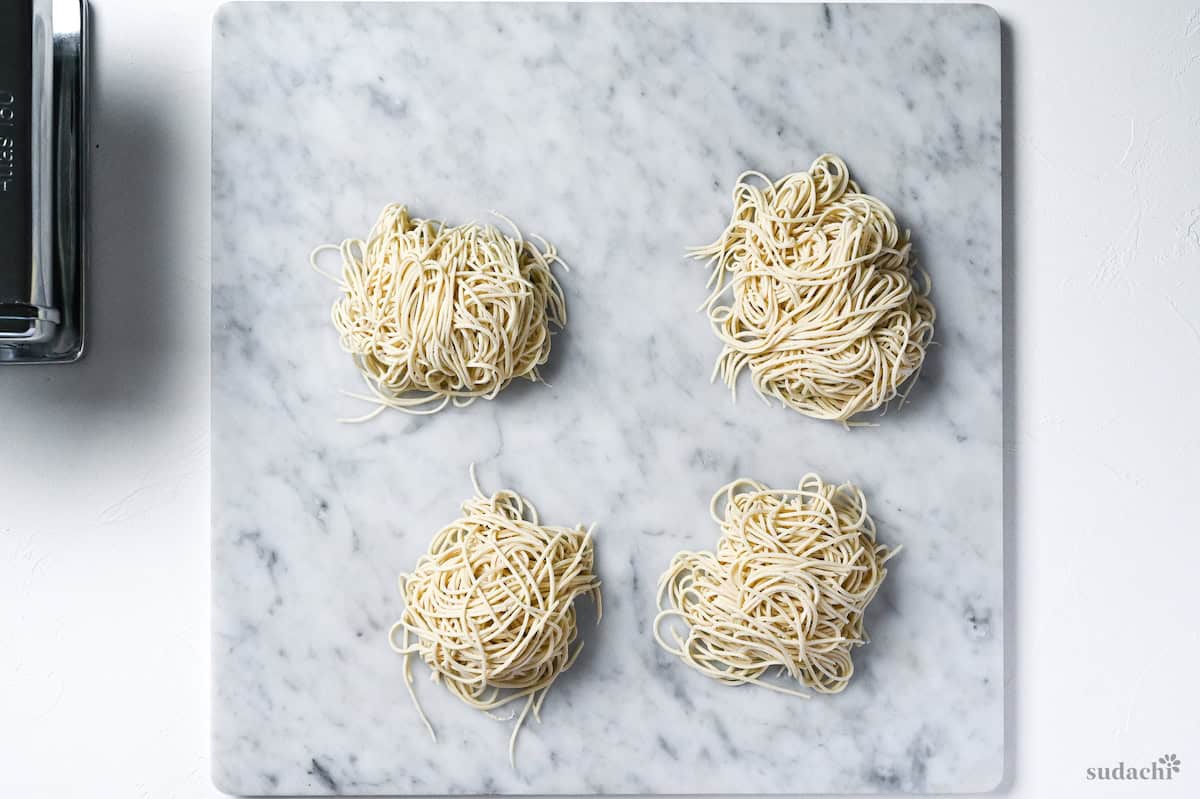 4 bundles of homemade ramen noodles on a marble kneading board